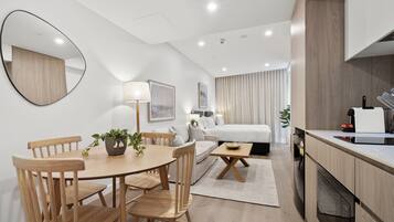 A modern hotel room with a wooden dining table, a sofa, a bed, and a kitchen area.