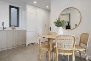 A modern kitchen with white cabinets, a round dining table, and four wicker chairs. - North Fremantle Apartment with Private BBQ (North Fremantle)