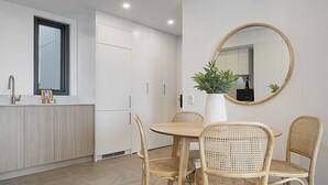 Una cocina moderna con armarios blancos, una mesa redonda para comer y cuatro sillas de mimbre.
