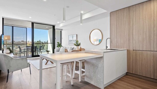 A modern kitchen with a central island, a dining area with chairs, and a large window offering a view.