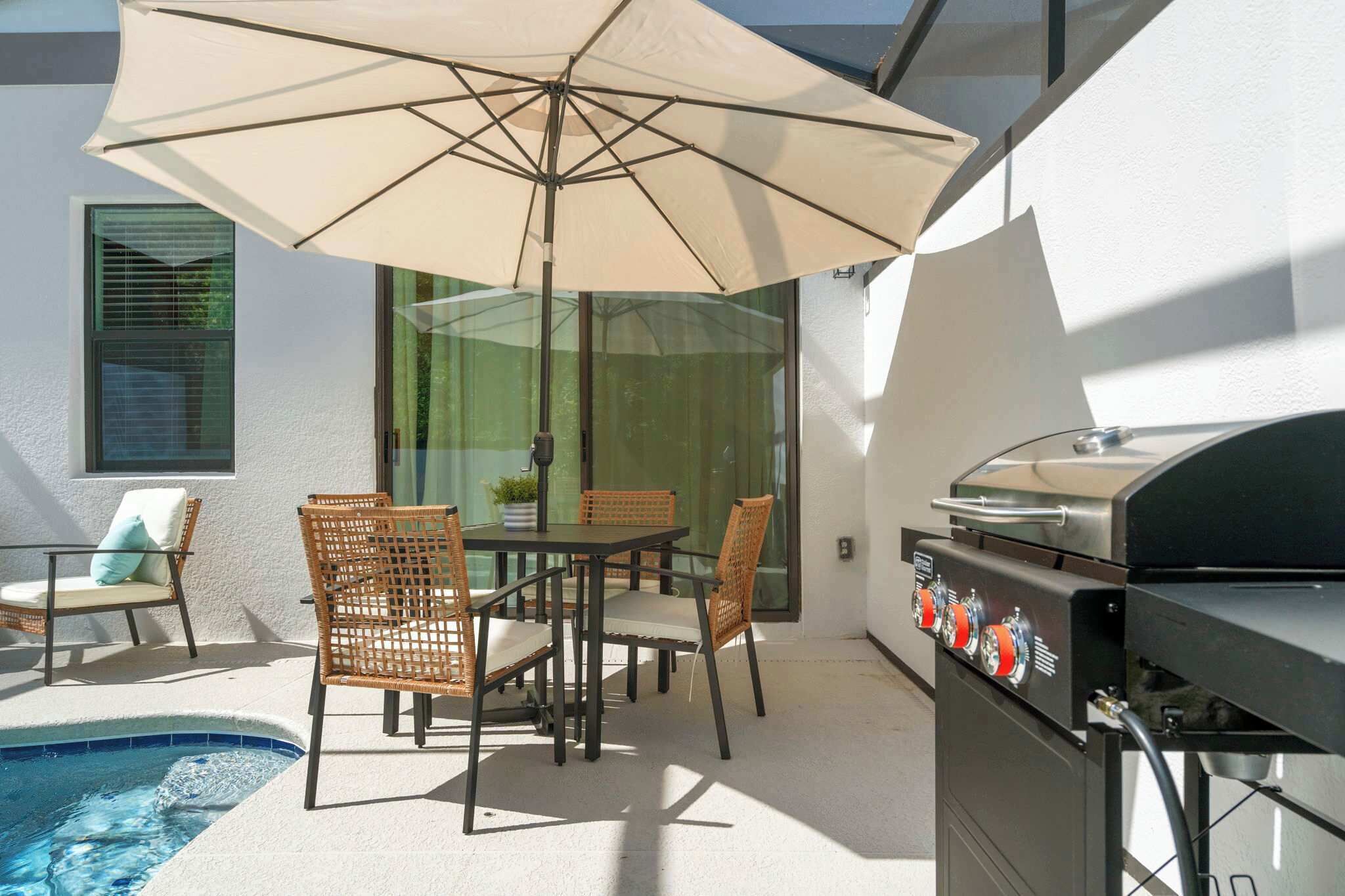 An outdoor patio with a table and chairs, a grill, and a swimming pool.