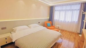 A hotel room with a large bed, a nightstand, an orange chair, a small table, and a window with curtains. - Yi Xian Ju Inn (Ya'an)