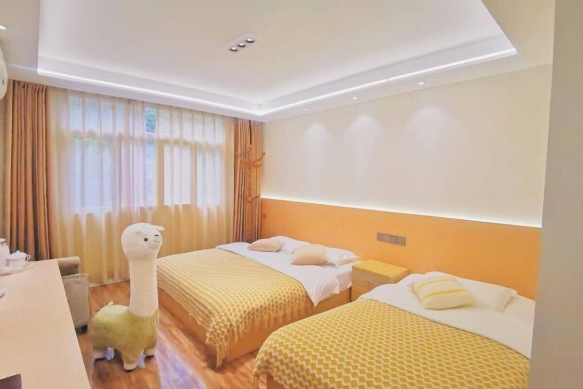 Quarto de hotel com duas camas, uma escrivaninha e um grande bicho de pelúcia.