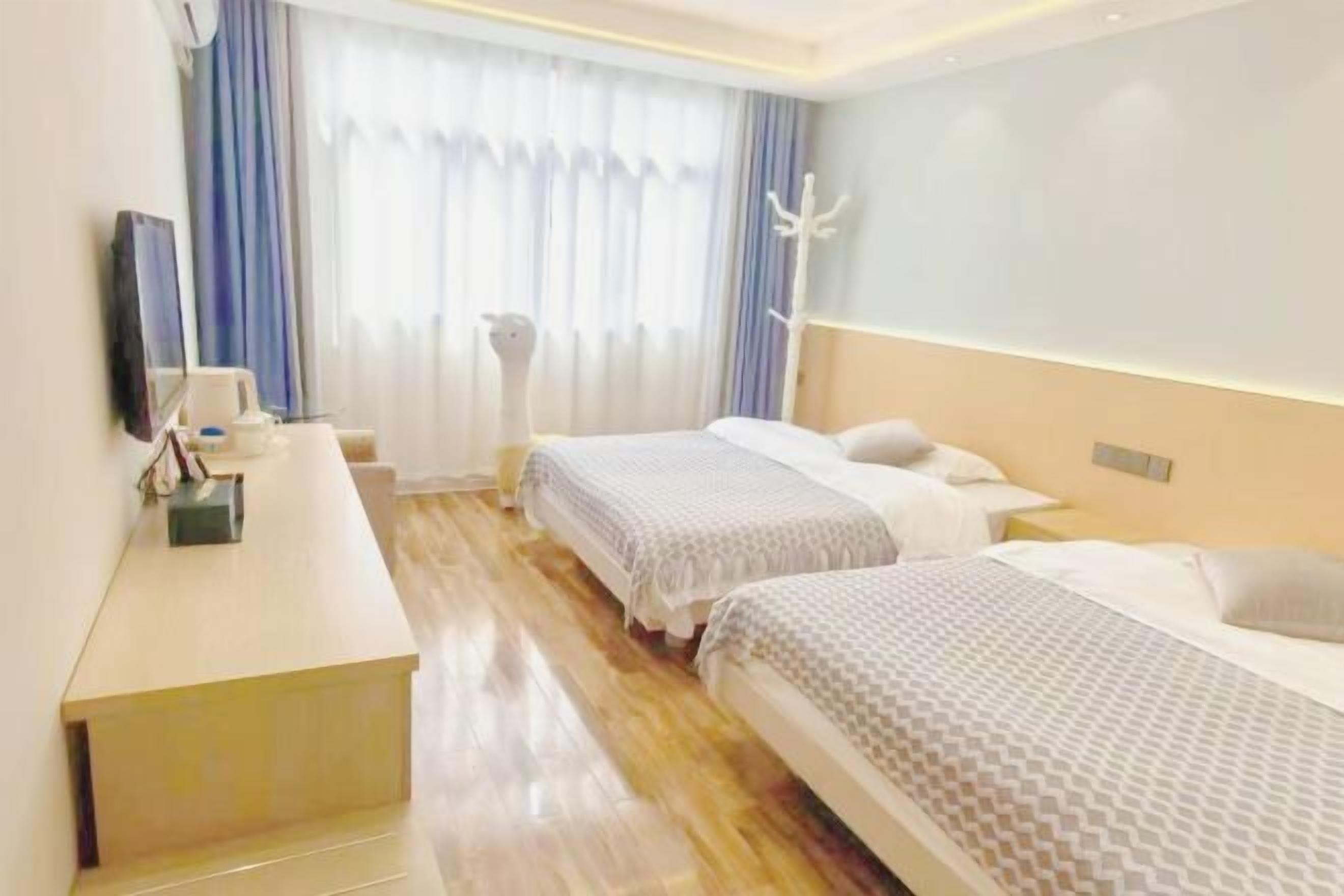 A hotel room with two beds, a desk, a chair, and a large window with curtains.
