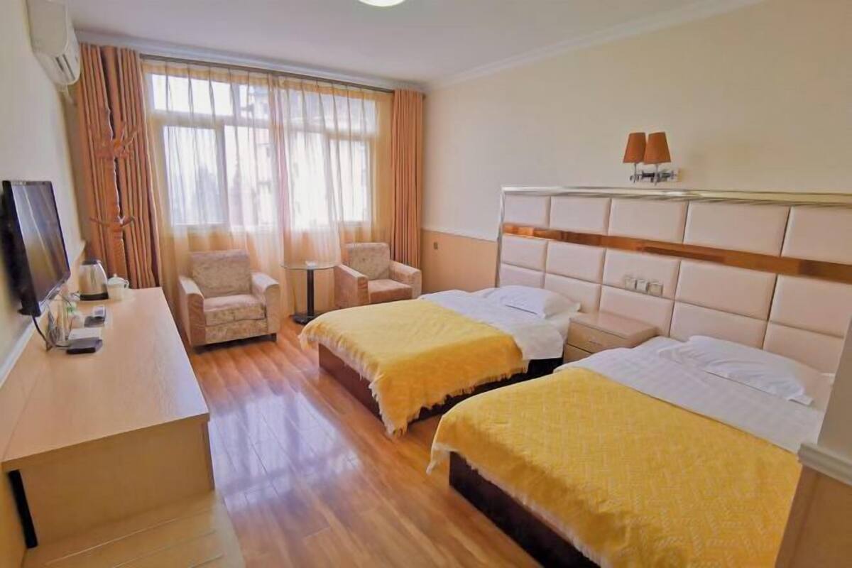 Quarto de hotel com duas camas, uma escrivaninha, uma cadeira e uma televisão.