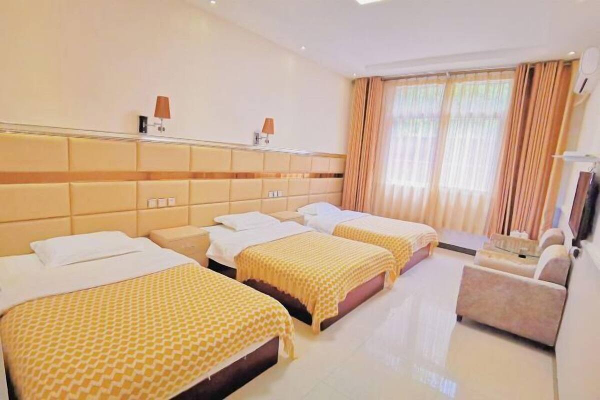 Quarto de hotel com três camas, um sofá, uma televisão e uma janela com cortinas.