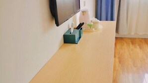 A room with a wooden floor, a flat-screen TV mounted on the wall, a small table with a green box, a white coffee maker, and a glass container. - Yi Xian Ju Inn (Ya'an)