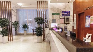 Un área de recepción moderna de hotel, con un mostrador de mármol, plantas en macetas y carteles informativos en la pared.