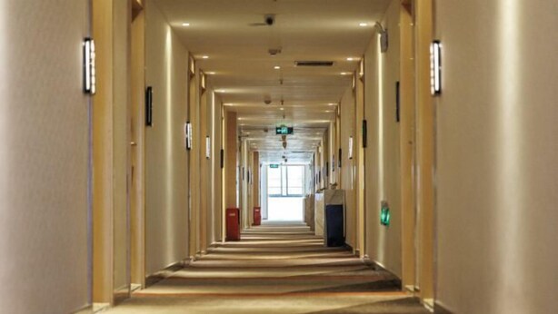 Un largo pasillo de hotel, estrecho, con piso alfombrado, puertas a ambos lados y luz en el techo.