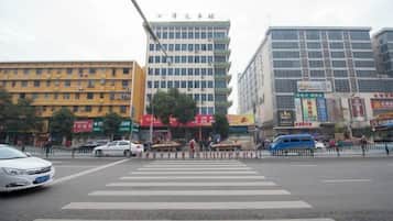 Una intersección urbana con varios edificios, incluyendo uno alto que tiene un letrero, y un paso de cebra.