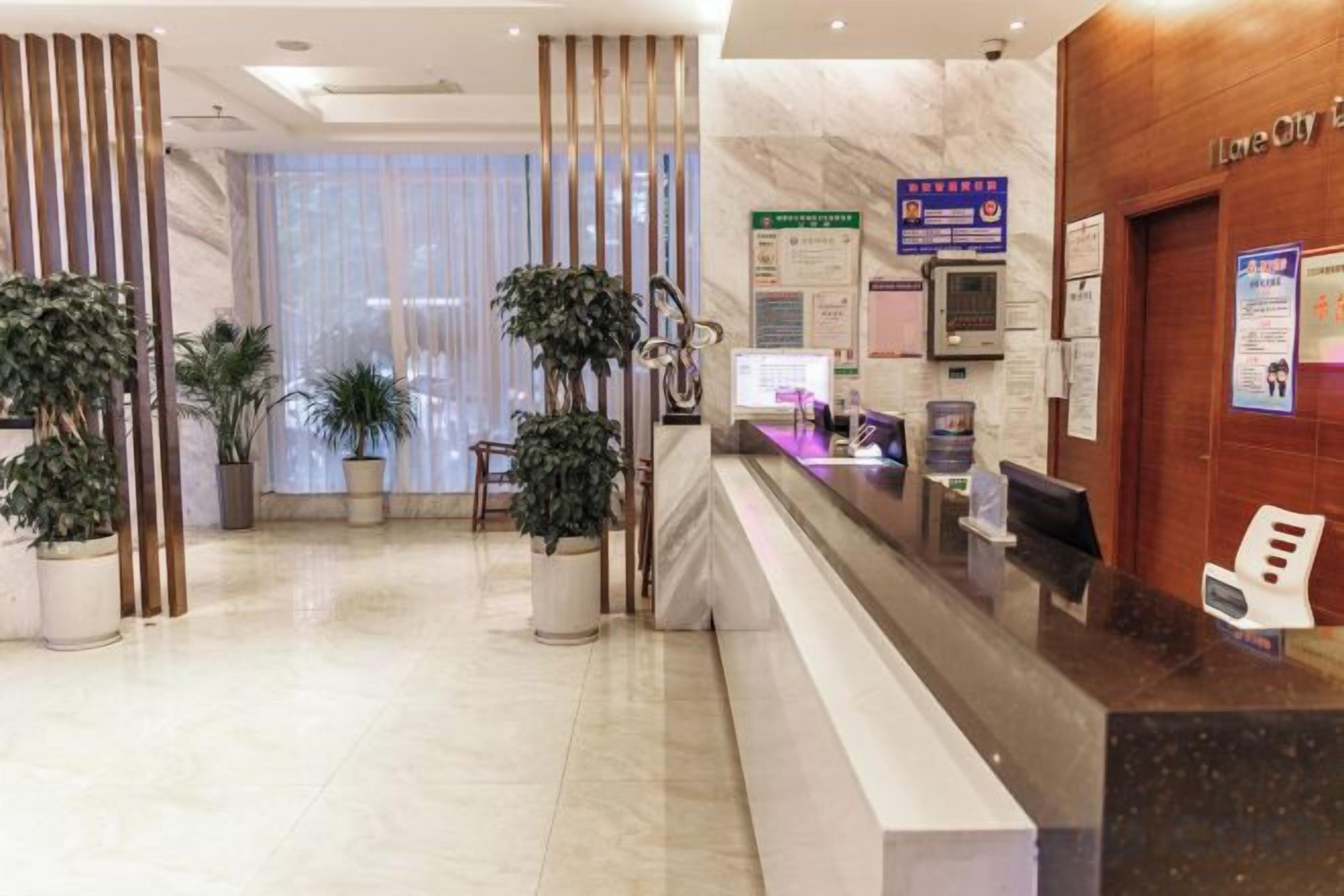 A hotel reception area with a marble floor, reception desk, potted plants, and a view of the city through large windows.