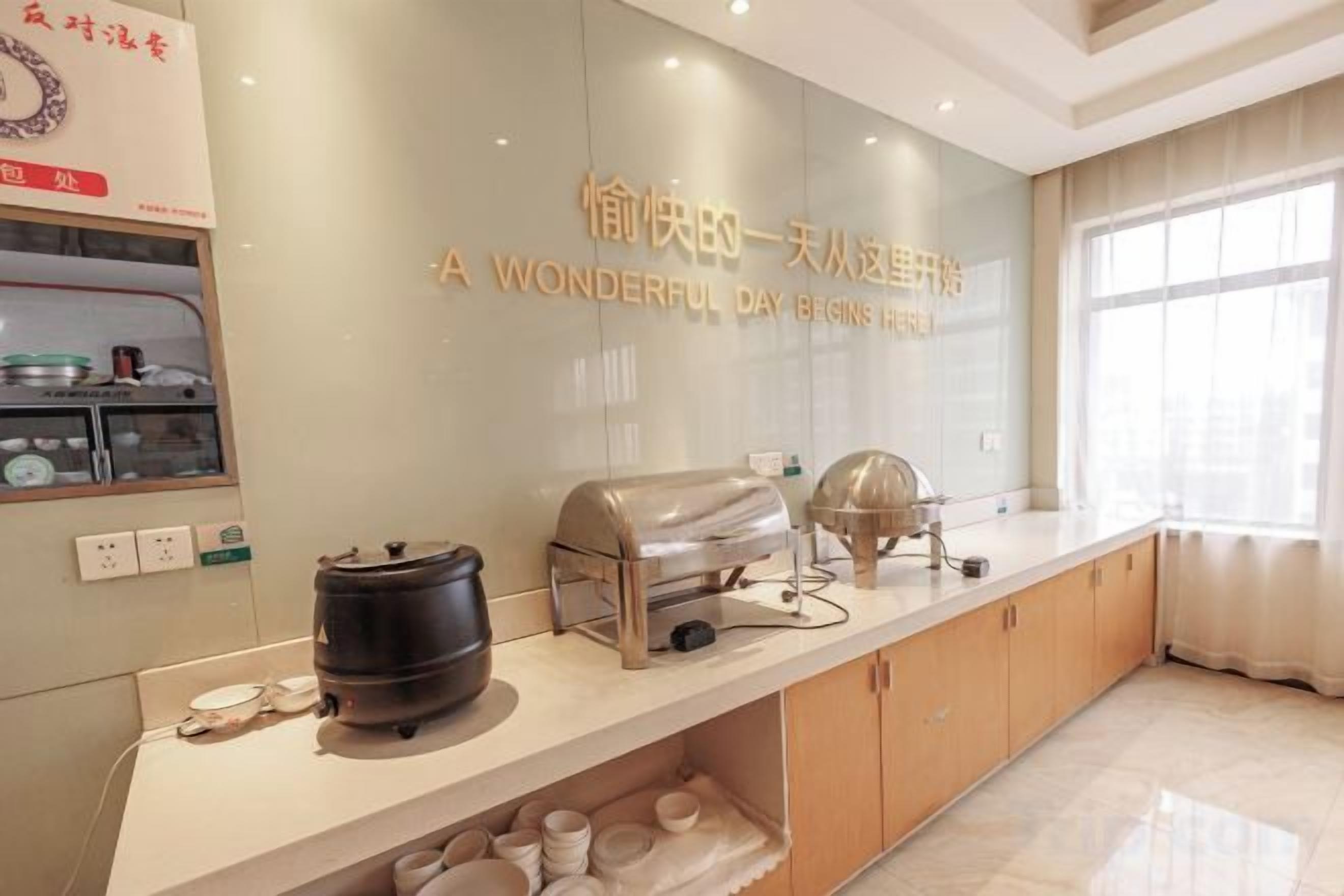 A kitchen with a countertop, a wall-mounted kettle, and a window with curtains.