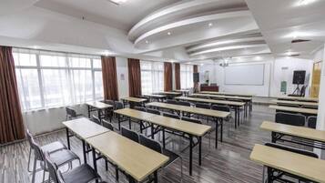 Un salón de conferencias con varias mesas y sillas, una pizarra y una pantalla de proyector.