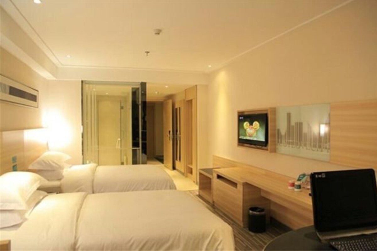 A hotel room with two beds, a desk with a laptop, a TV, and a door leading to a hallway.