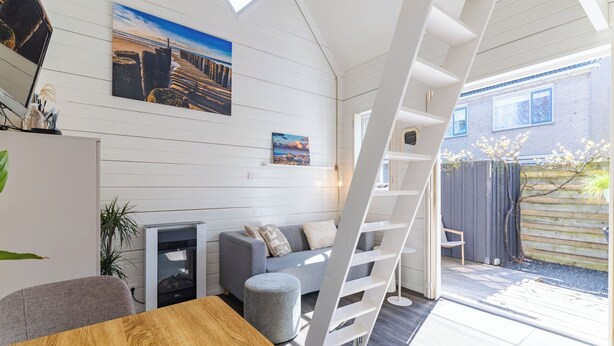 A modern interior with a wooden dining table, grey sofa, and a white ladder leading to an outdoor area. - Residence Domburg by Interhome (Domburg)