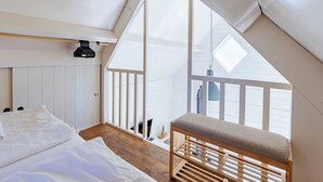 A bedroom with a sloped ceiling, a bed, a bench, and a view through a window. - Residence Domburg by Interhome (Domburg)