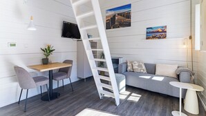 A modern interior with a wooden floor, a sofa, a dining table with chairs, a white ladder, and a TV mounted on the wall. - Residence Domburg by Interhome (Domburg)