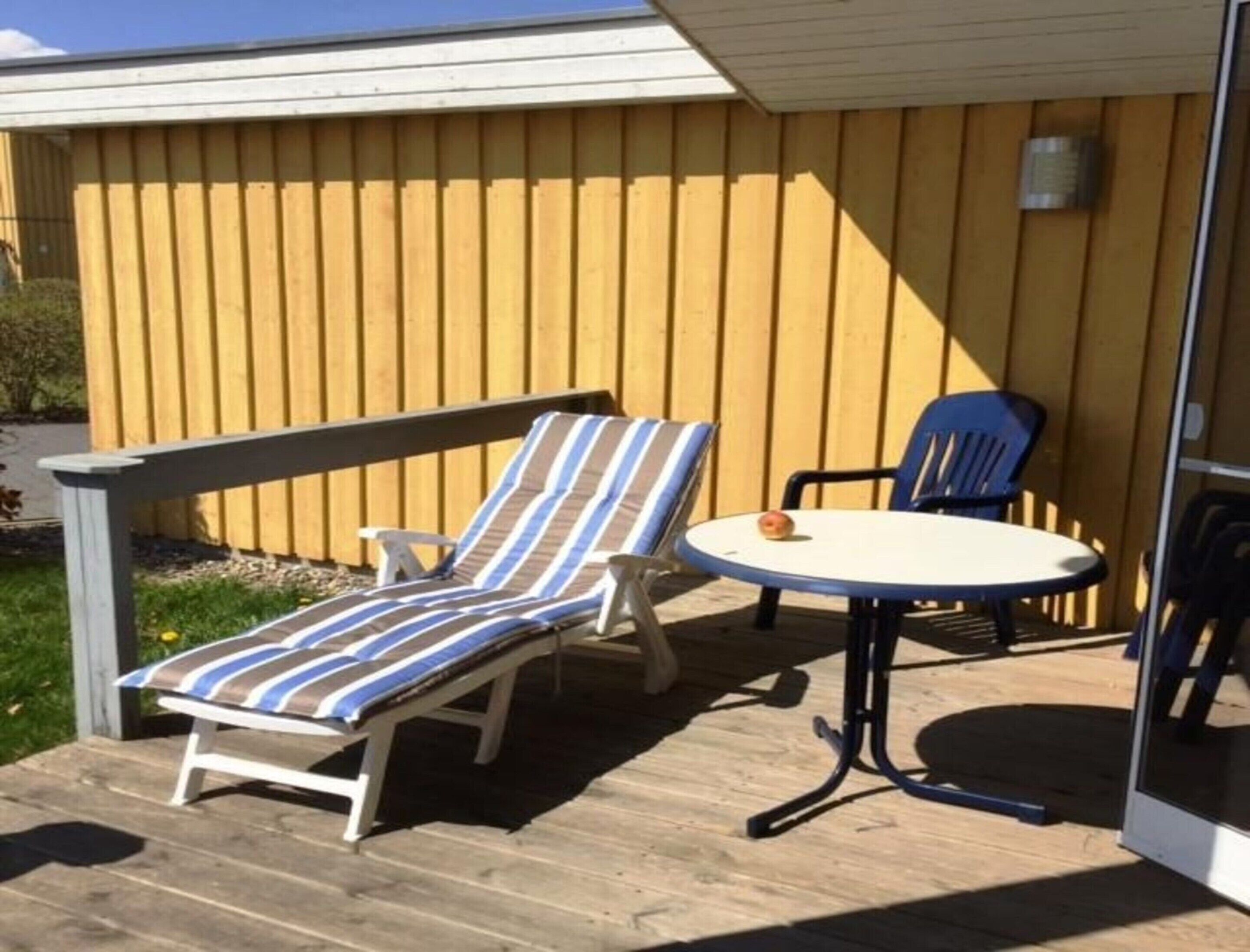 A deck with a lounge chair, a striped cushion, a small table, and a chair.