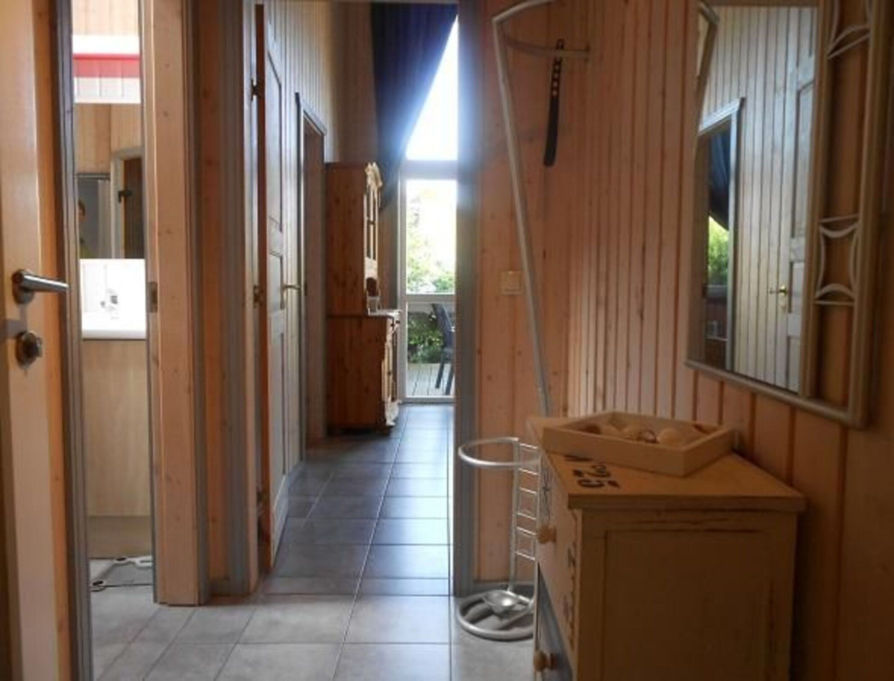 A hallway with wooden walls, a tiled floor, and a view to the outside.