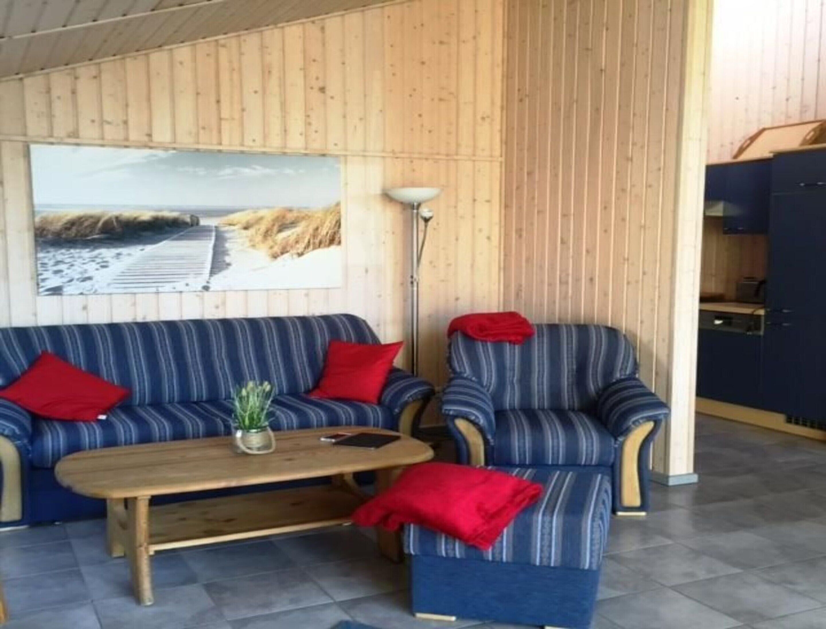 Et værelse med en trævæg, en sofa, en lænestol, et sofabord og et maleri af en strand.