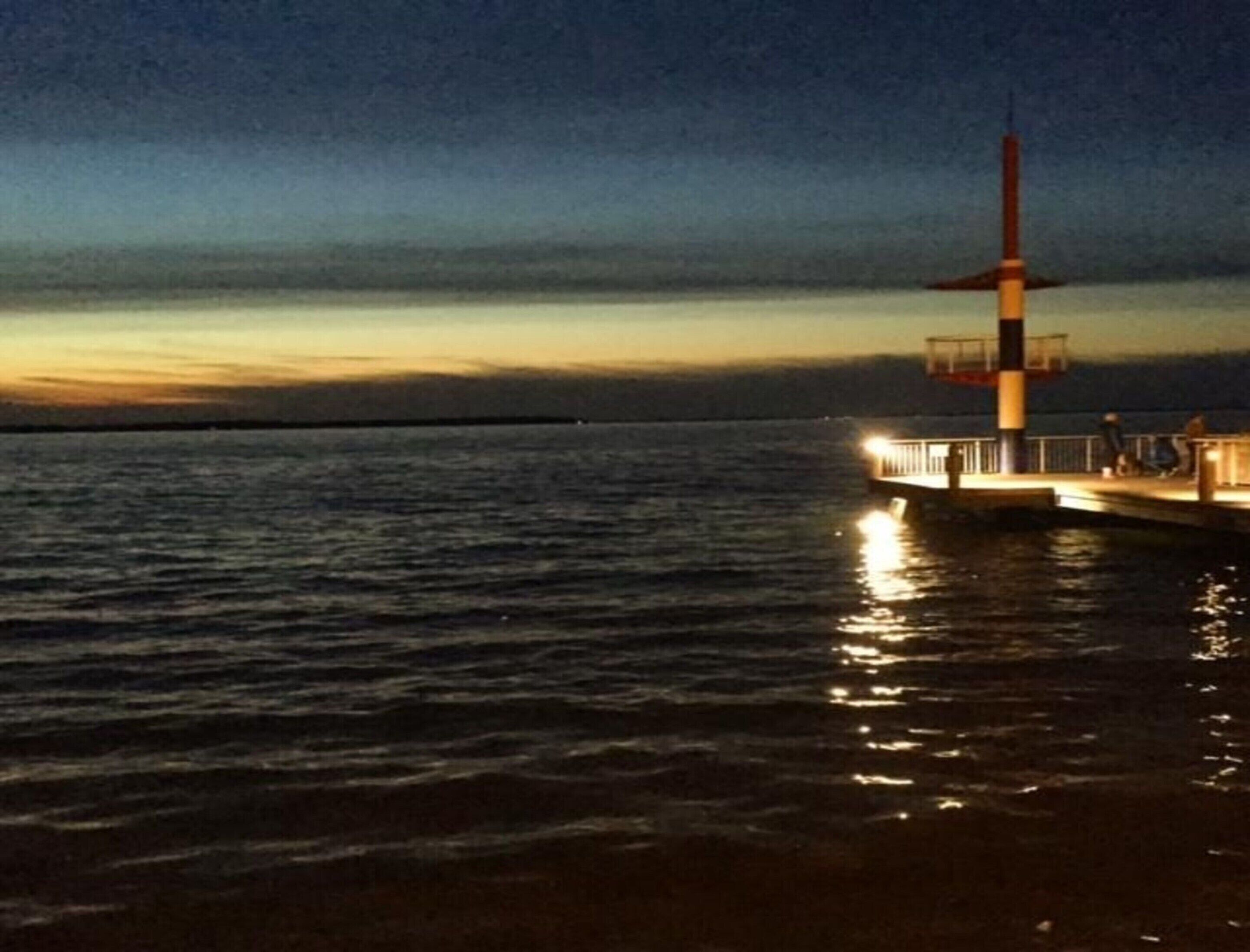 Majakka auringonlaskun aikaan, tyyni meri ja selkeä horisontti.