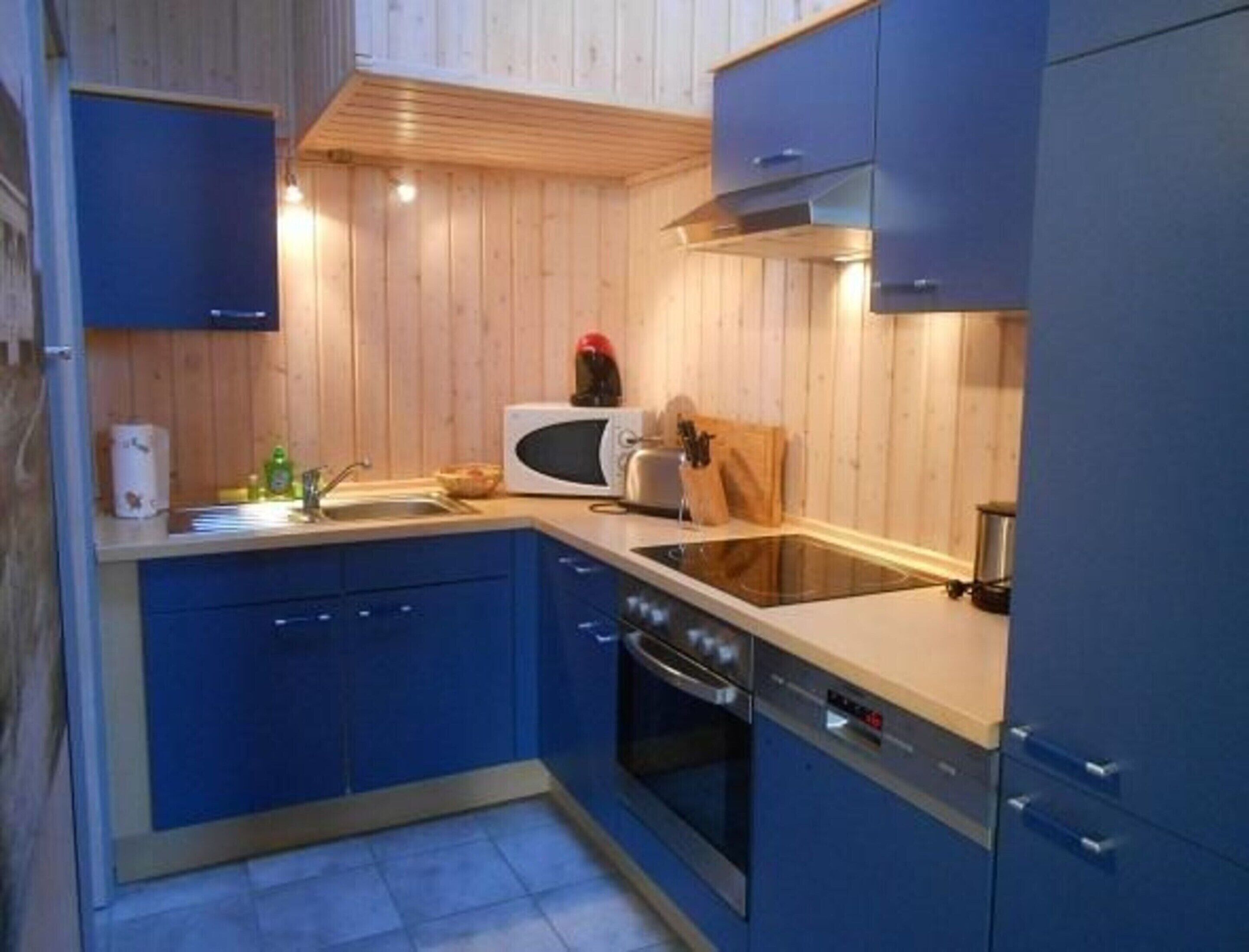 Een kleine keuken met blauwe kastjes, een magnetron, een spoelbak en een fornuis.