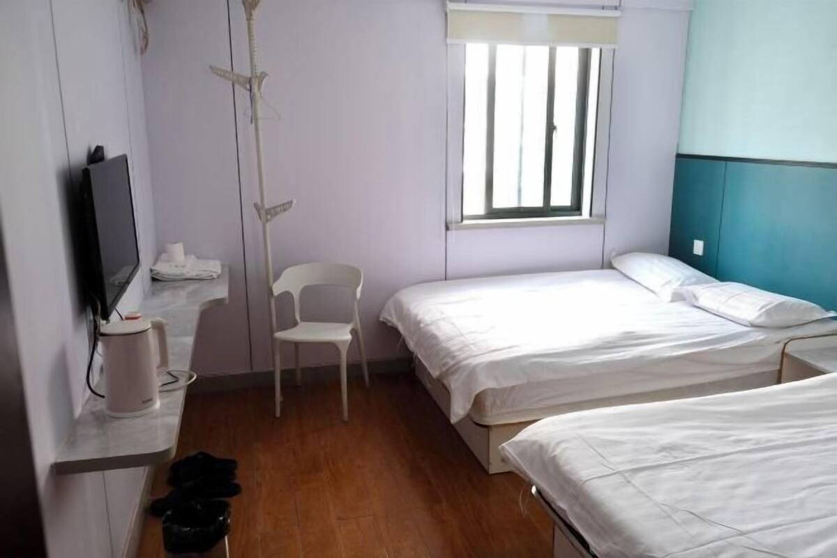 A room with two beds, a TV, a chair, and a window.