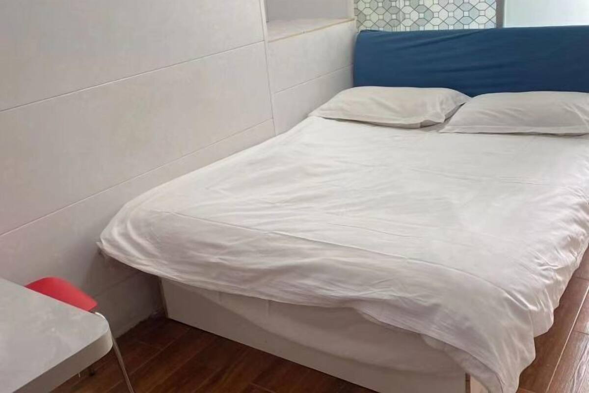 A bed with white bedding, a blue headboard, and a red pillow on a wooden floor.