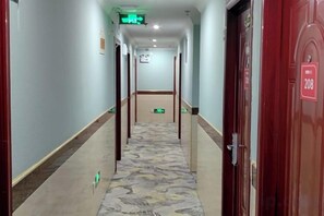 A hotel corridor with a patterned carpet, doors, and emergency exit signs. - Zhexin Business Hotel (Shanghai)