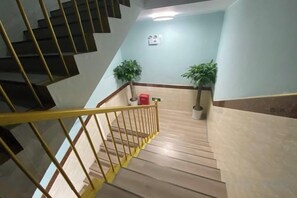 A staircase with a yellow handrail leading to a landing with two potted plants and a light switch on the wall. - Zhexin Business Hotel (Shanghai)