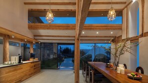 A modern kitchen with wooden beams, a long counter, and a dining area with a table and chairs. - Lanxiu Homestay (Lijiang)