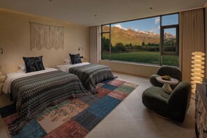 A bedroom with two beds, a large window with a mountain view, a green armchair, and a small table with fruit. - Lanxiu Homestay (Lijiang)