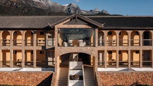 A hotel with a central atrium, multiple balconies, and a mountainous backdrop. - Lanxiu Homestay (Lijiang)