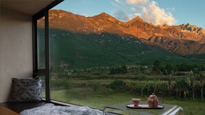 A room with a large window offering a mountain view, a cozy seating area with a fur rug, and a table with a teapot and cup. - Lanxiu Homestay (Lijiang)