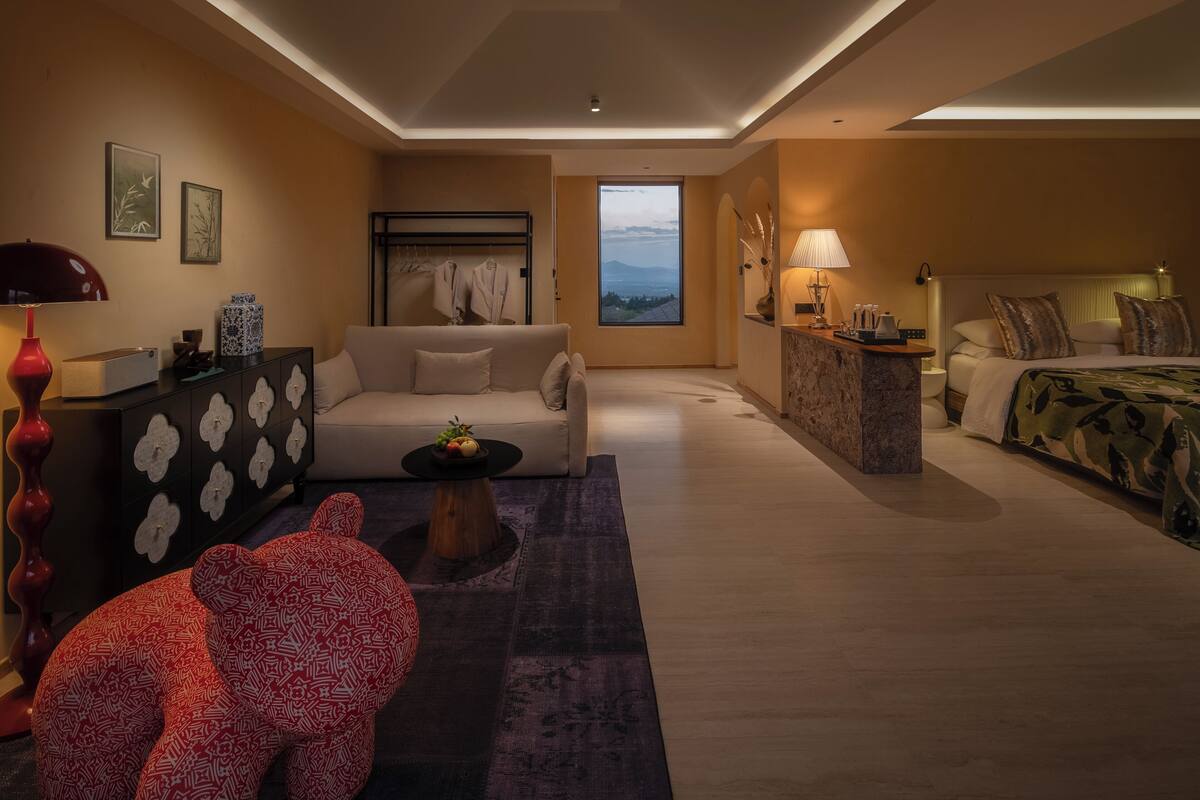A modern hotel room with a sofa, a bed, a small table, and a view of the mountains.