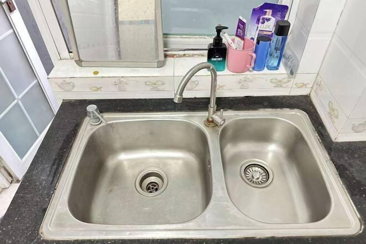 A kitchen with a double stainless steel sink, a window, and toiletries on the counter.
