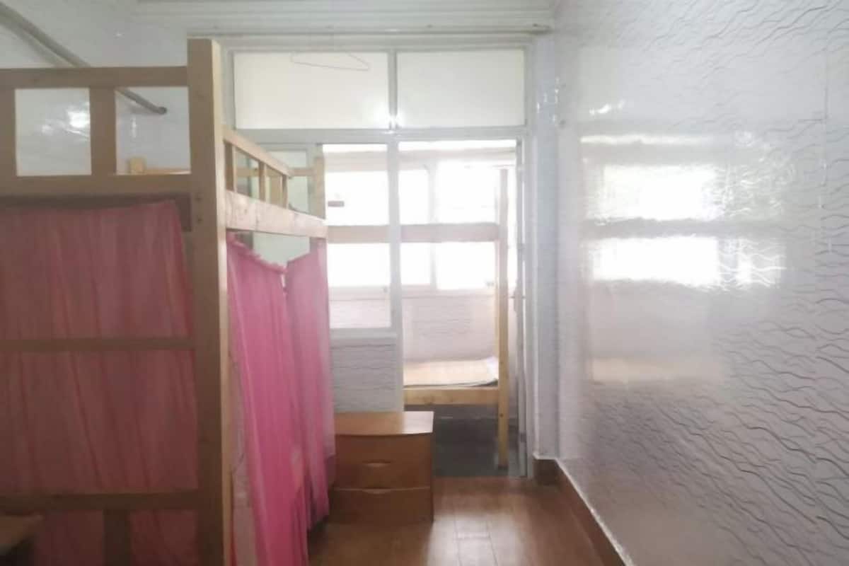 A room with a bunk bed, a small wooden desk, and a window with curtains.