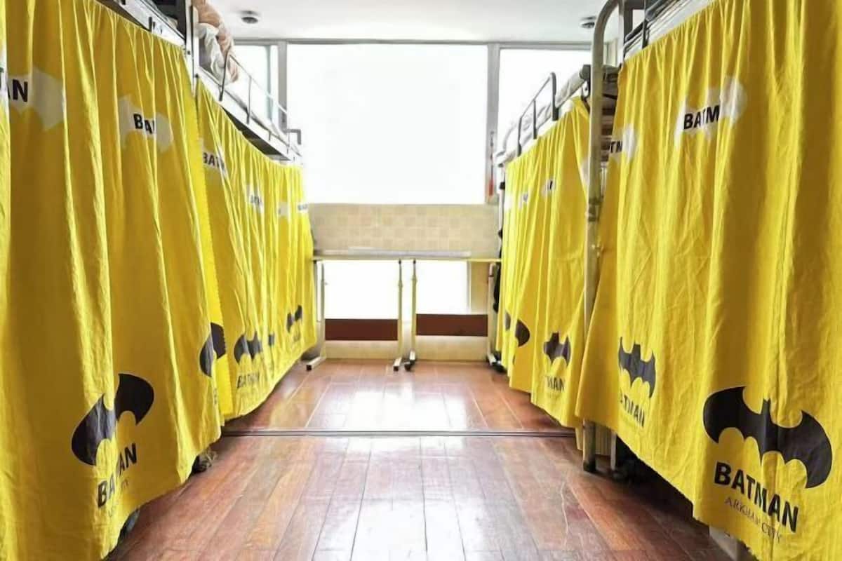 A row of bunk beds with yellow curtains featuring a Batman logo, a wooden floor, and a window in the background.