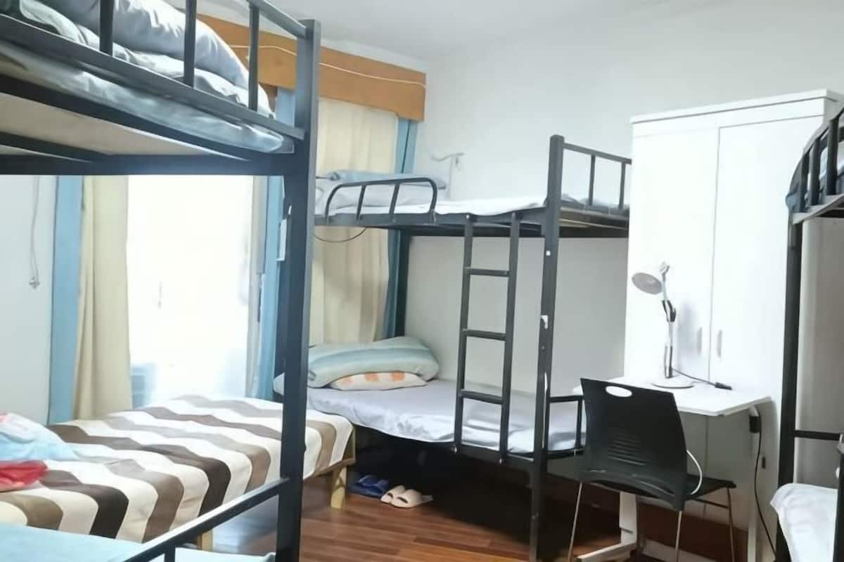 A bunk bed room with a desk and chair, a wardrobe, and a window with curtains.