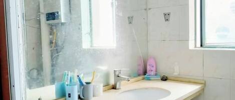 Un baño con lavamanos, espejo y ventana. Hay cepillos de dientes y pasta dental en un portalapices.