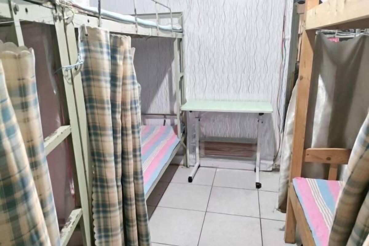 A dormitory room with bunk beds, a small table, and a chair.