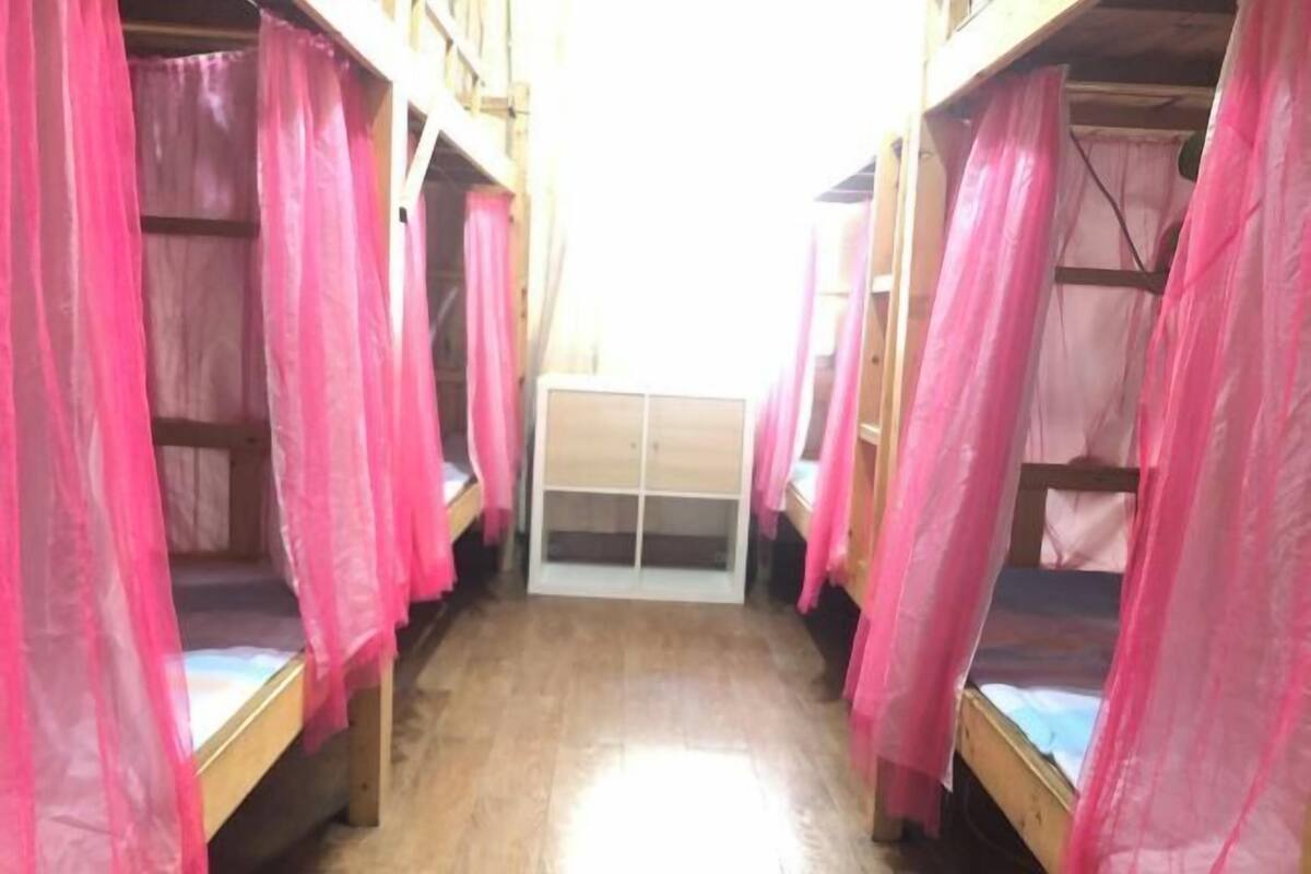 A narrow corridor with bunk beds on either side, a central door, and pink curtains.