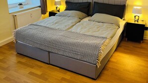 Une chambre à coucher avec un grand lit, deux tables de chevet avec des lampes, une fenêtre avec des stores et un radiateur.