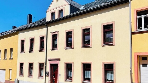 Une rangée de bâtiments jaunes, avec des fenêtres à encadrement rouge et une porte rouge au centre.