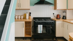 A kitchen with a black stove, white cabinets, and a teal backsplash.
