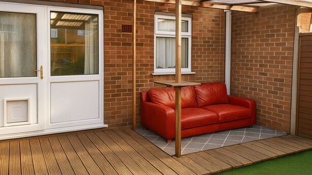 A covered patio area with a red leather sofa, a small table, and a wooden deck.