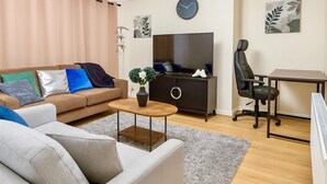 A modern living room with a sofa, a coffee table, a TV, a desk, and a chair.