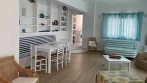 A living room with a striped sofa, a dining table with chairs, a wicker chair, and a small table with a book. - Villa Omega in Kokkali, Leros (Kokkali)