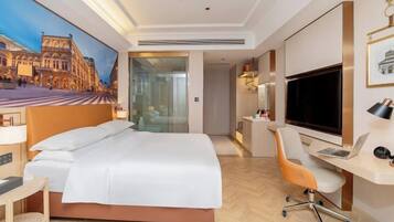 A hotel room with a bed, desk, chair, TV, and a painting on the wall.