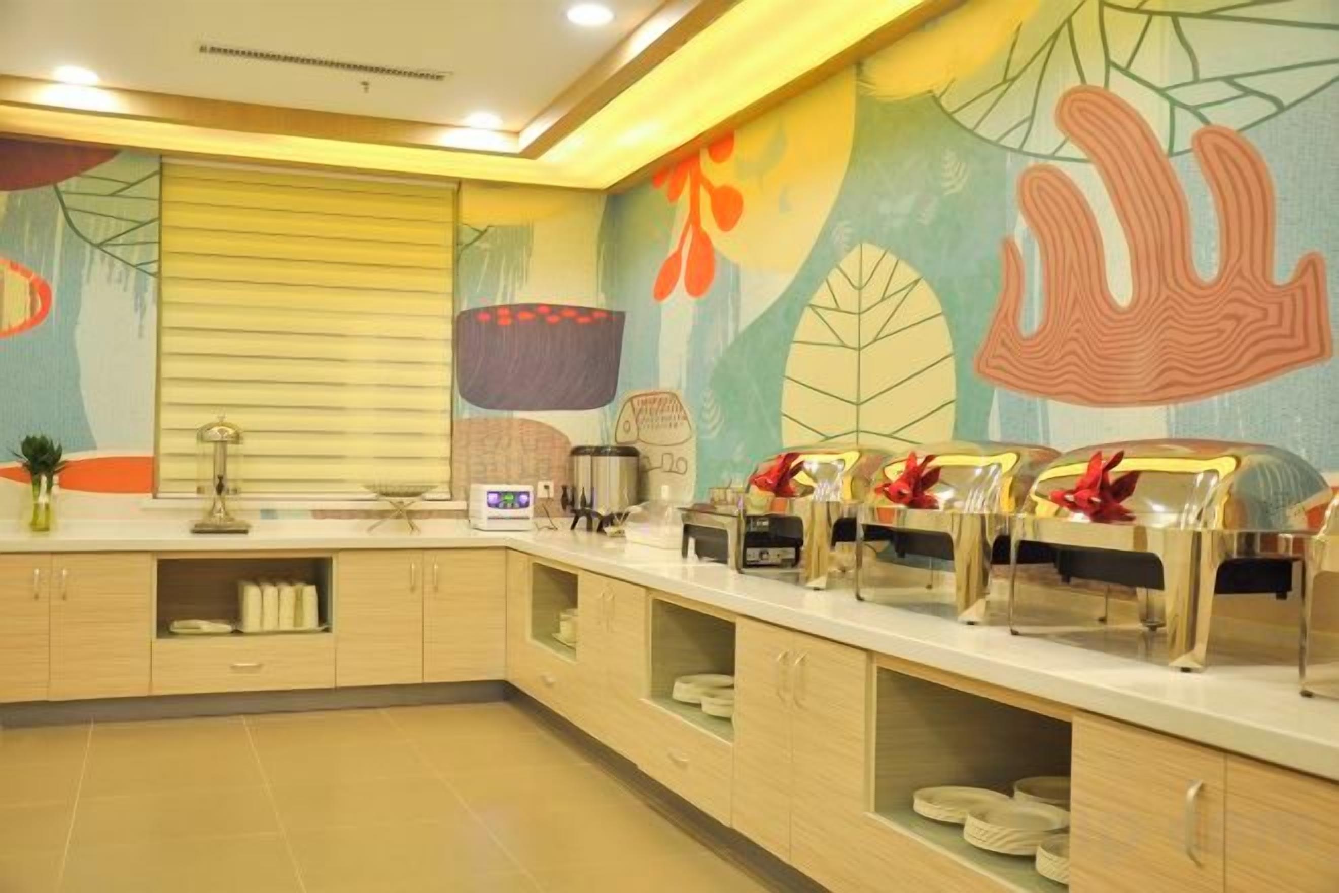 A hotel kitchen with a long counter, various appliances, and a decorative mural on the wall.